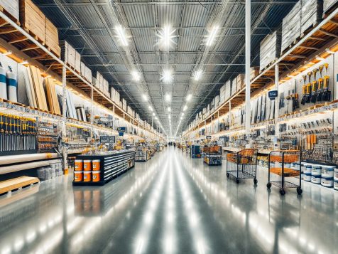 High-resolution photograph of a brightly lit home improvement store with wide aisles, neatly organized tools, lumber, paint cans, and hardware, creating a sharp and clean shopping environment.