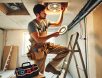 A skilled electrician installing recessed lighting in a residential home, standing on a ladder with tools and exposed wiring, demonstrating precision and expertise in electrical installations.