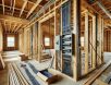 High-resolution photograph of an unfinished home under construction, featuring exposed electrical wiring, wooden framing, and scattered building materials in a well-lit, sharp, and detailed setting.