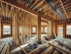 High-resolution photograph of an unfinished home under construction, featuring exposed electrical wiring, wooden framing, and scattered building materials in a well-lit, sharp, and detailed setting.